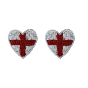 Könnte beinhalten: Zwei kleine herzförmige Aufnäher mit der Flagge Englands darauf gestickt. Die Aufnäher sind weiß mit einem roten Kreuz.