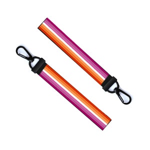 May include: Two black keychains with a lesbian pride flag design. The flag has stripes of pink, orange, white, and light pink.