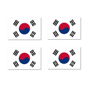 May include: Four white rectangular stickers with the South Korean flag printed on them. The flag features a red and blue circle with a yin-yang symbol in the center, surrounded by four black trigrams.