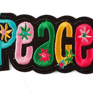 Op de afbeelding: Een kleurrijk geborduurd patch met het woord "Peace" in een retro stijl. De letters zijn zwart omrand en gevuld met verschillende kleuren, waaronder roze, groen, blauw en geel. Elke letter heeft een klein bloemenontwerp dat erin is geborduurd.