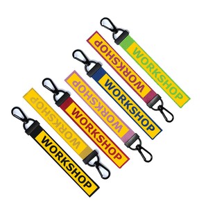 May include: Five colorful keychains with black metal rings. Each keychain has the word "WORKSHOP" printed on it in a different color and font style. The keychains are yellow, green, blue, pink, and red.