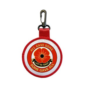 May include: A circular keychain featuring a poppy design, with the text "ALL GAVE SOME, SOME GAVE ALL" and "LEST WE FORGET". The keychain has a red strap and a black clip. The design is red, white, and black.