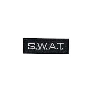 Puede incluir: Parche rectangular negro con texto bordado en blanco que dice "S.W.A.T."