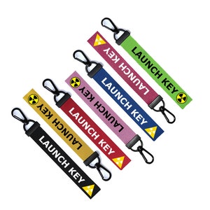 Peut inclure: Cinq porte-clés colorés avec des anneaux métalliques noirs et un symbole de radiation jaune. Chaque porte-clés porte l'inscription "LAUNCH KEY" en noir.