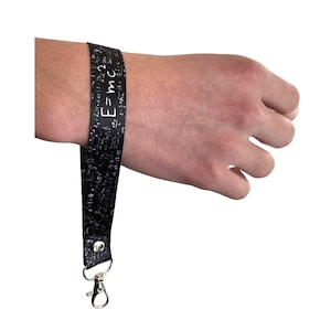 Könnte beinhalten: Schwarzes Lanyard mit einem weißen Aufdruck von mathematischen Gleichungen und der Formel "E=mc^2". Das Lanyard hat einen silbernen Clip.