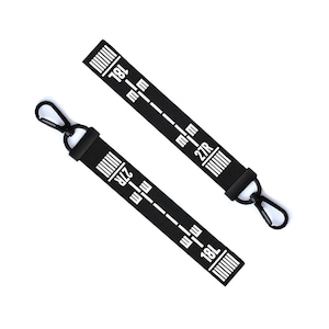 Puede incluir: Dos etiquetas de equipaje negras con texto y marcas blancas. Las etiquetas tienen un clip negro y dicen "18L" y "27R".
