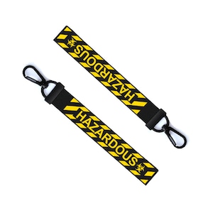 May include: Two black keychains with yellow and black striped bands. The bands have the word "HAZARDOUS" printed in yellow letters and a biohazard symbol. The keychains have a black metal hook.