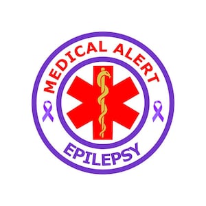 Puede incluir: Un emblema circular de alerta médica con una estrella de la vida roja en el centro, un caduceo dorado y las palabras "MEDICAL ALERT" y "EPILEPSY" en un círculo morado. Dos lazos de concienciación morados a cada lado.