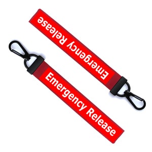 Op de afbeelding: Twee rode stoffen lanyards met de woorden "Emergency Release" in het wit gedrukt. Elke lanyard heeft een zwarte metalen clip en een zwarte stoffen lus. De lanyards staan schuin tegen een witte achtergrond.