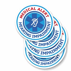 May include: Several circular stickers with a white background. Each sticker has a blue and white border with the words "MEDICAL ALERT" in red and "HEARING IMPAIRMENT" in blue. The centre features a blue star and a white ear symbol.