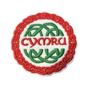 Può includere: Una toppa rotonda bianca ricamata con un bordo rosso a nodo celtico. Il centro presenta un disegno di nodo celtico verde con la parola "CYMRU" in lettere rosse.