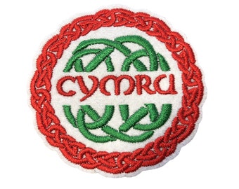May include: A white, round embroidered patch with a red Celtic knot border. The center features a green Celtic knot design with the word "CYMRU" in red lettering.