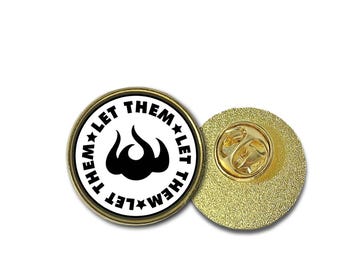 May include: A gold-colored pin with a white circle and black text that reads "Let Them Let Them" with a black flame design in the center.