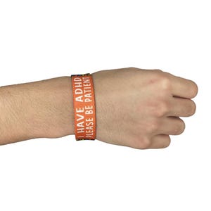 May include: Orange wristband with the text "I have ADHD Please be patient" in white.