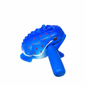 Peut inclure: Une grenouille en bois bleue avec des points rouges et un b&acirc;ton bleu dans sa bouche. La grenouille est un instrument de musique.