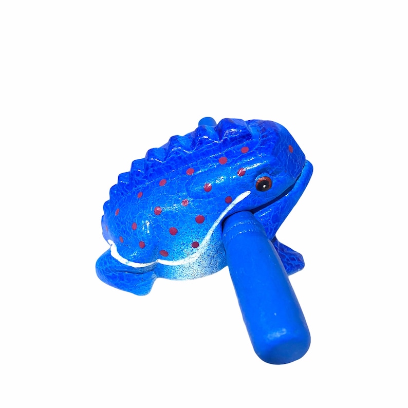 Peut inclure: Une grenouille en bois bleue avec des points rouges et un b&acirc;ton bleu dans sa bouche. La grenouille est un instrument de musique.