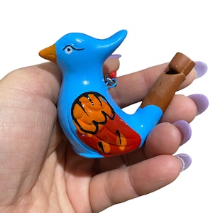 Puede incluir: Un silbato de cer&aacute;mica azul en forma de p&aacute;jaro con detalles pintados de naranja y rojo. El silbato se sostiene en una mano.