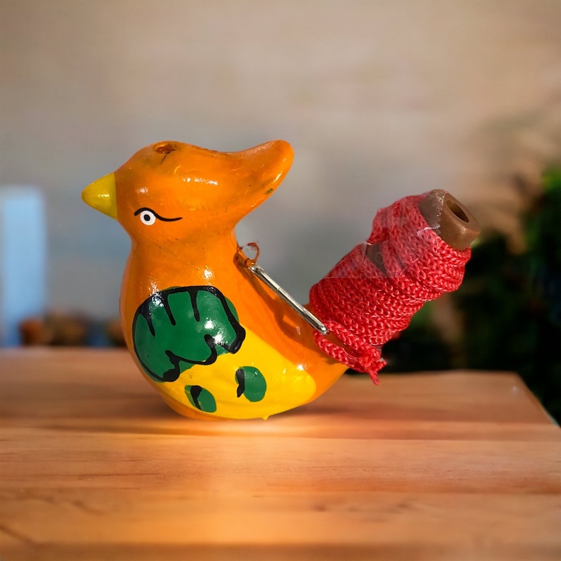 Puede incluir: Un silbato de cer&aacute;mica con forma de p&aacute;jaro pintado en naranja, amarillo, verde y rojo. El silbato tiene una cuerda roja atada.