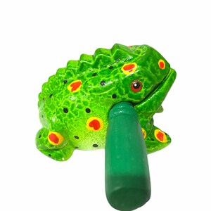 Peut inclure: Instrument de musique en bois en forme de grenouille verte avec des taches rouges et jaunes. La grenouille a un b&acirc;ton vert qui sert &agrave; frapper le corps de la grenouille pour faire du bruit.