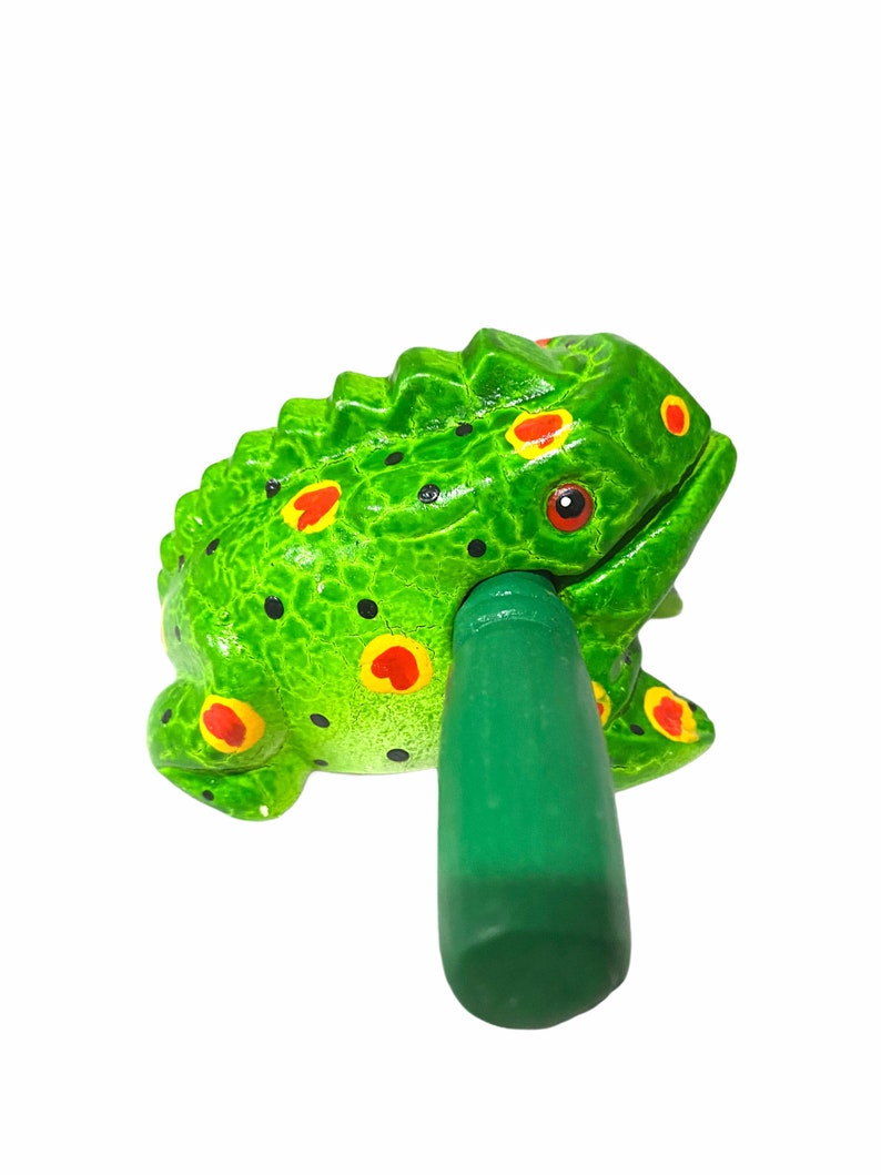 Peut inclure: Instrument de musique en bois en forme de grenouille verte avec des taches rouges et jaunes. La grenouille a un b&acirc;ton vert qui sert &agrave; frapper le corps de la grenouille pour faire du bruit.