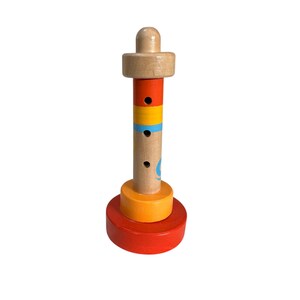 May include: A wooden toy whistle shaped like a lighthouse with red, orange, and yellow rings. The whistle has three holes and a blue and white design on the side.