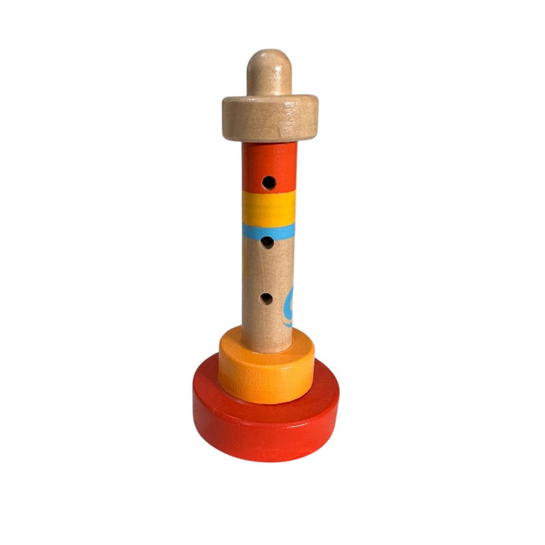 May include: A wooden toy whistle shaped like a lighthouse with red, orange, and yellow rings. The whistle has three holes and a blue and white design on the side.