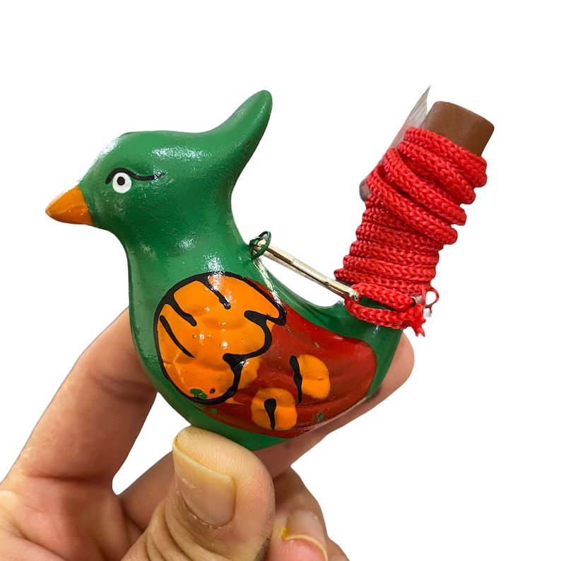 Puede incluir: Un silbato de p&aacute;jaro verde y rojo con detalles pintados de naranja y rojo. El silbato tiene una cuerda roja atada a la parte posterior.