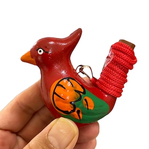 Puede incluir: Un silbato de p&aacute;jaro de cer&aacute;mica rojo, naranja y verde con una cuerda roja atada alrededor del cuello.