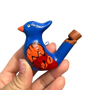 Puede incluir: Un silbato de p&aacute;jaro azul y naranja con un agujero de silbato marr&oacute;n. El p&aacute;jaro tiene un dise&ntilde;o rojo y naranja en su cuerpo.