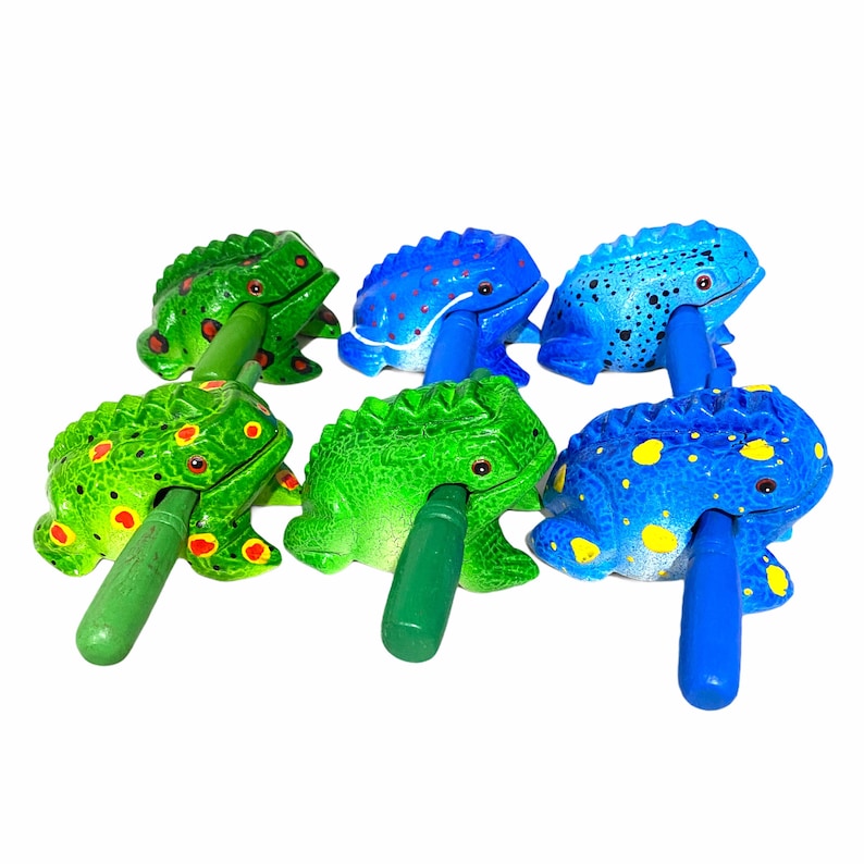 Peut inclure: Six hochets en forme de grenouille en bois peints en vert et bleu. Chaque grenouille a un motif diff&eacute;rent et un b&acirc;ton en bois pour la secouer.