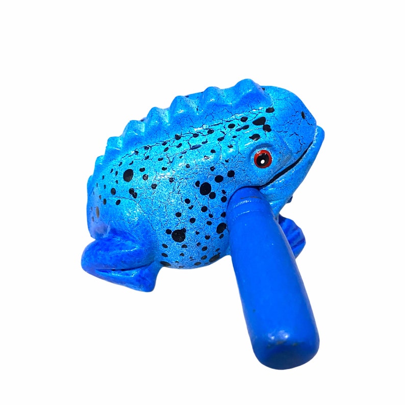 Peut inclure: Un instrument de musique en bois en forme de grenouille bleue avec une surface textur&eacute;e et des taches noires. La grenouille a un &oelig;il rouge et une poign&eacute;e bleue.