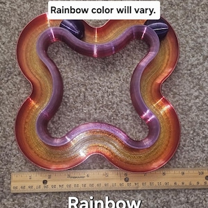 May include: A rainbow-colored, four-loop track with two purple spheres. The track is made of a metallic material with gold, orange, and purple hues. The text "Rainbow color will vary" and "Rainbow" are visible.