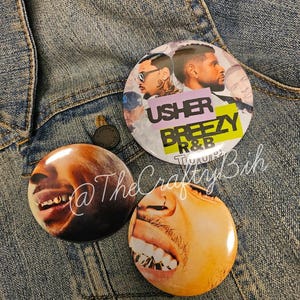 May include: Three round buttons with images of Usher and Chris Brown. One button has the text "Usher Breezy R&B Tour". The buttons are on a denim jacket.