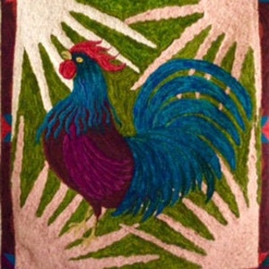 May include: A colorful embroidered wall hanging featuring a rooster with a red comb, blue body, and purple tail feathers. The rooster is surrounded by a green and pink geometric pattern.