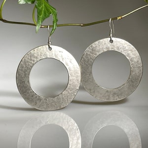 May include: A pair of silver hoop earrings with a hammered texture. The earrings are large and circular, with a diameter of approximately 5 cm.