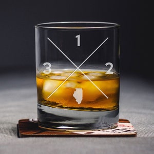 May include: A clear glass tumbler with an etched design of a cross with the numbers 1, 2, 3, and the outline of the state of Illinois. The glass is filled with amber liquid and ice cubes.