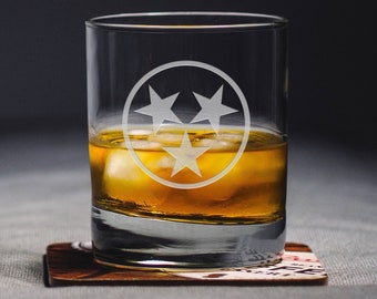 May include: A clear glass tumbler with a frosted design of the state of Tennessee's three stars inside a circle. The glass is filled with amber liquid and ice cubes.