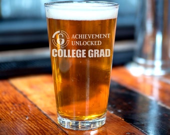 May include: A frosted glass beer mug with the text "Achievement Unlocked College Grad" and a graphic of a padlock with the number 6 on it.