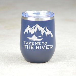 Puede incluir: Un vaso de acero inoxidable azul con un dise&ntilde;o blanco de monta&ntilde;as, &aacute;rboles y una persona en kayak. El texto "Take me to the river" est&aacute; impreso en el vaso.