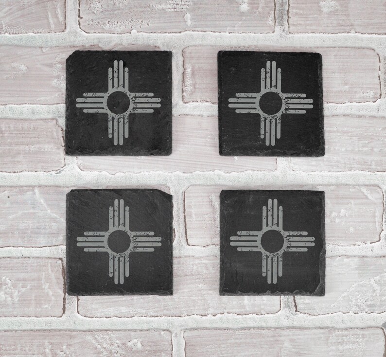 May include: Four black slate coasters with a white Zia symbol, the state symbol of New Mexico, on each coaster.