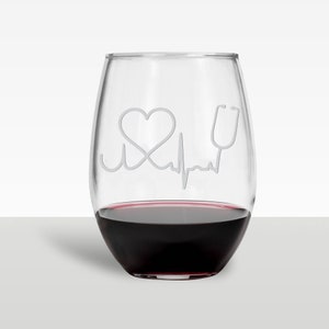 Może przedstawiać: Szklanka do wina z przezroczystego szkła z wygrawerowanym sercem, stetoskopem i linią EKG. Szklanka jest wypełniona czerwonym winem.