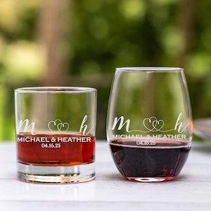 May include: Two personalized glasses, one a wine glass and one a rocks glass, with the initials "M" and "H" connected by two hearts and the text "Michael & Heather 04.16.25" etched on each.