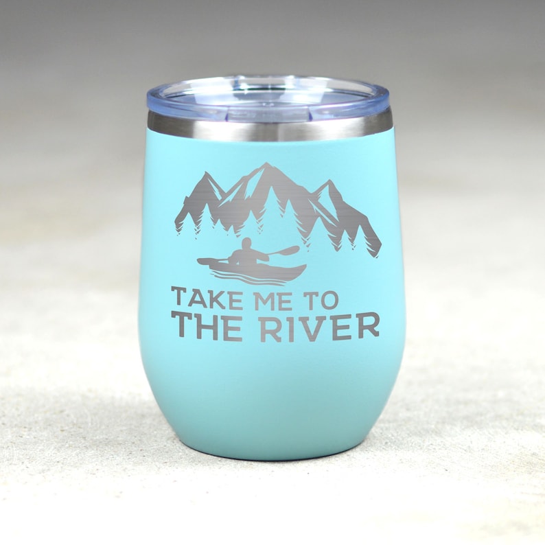 Puede incluir: Un vaso de acero inoxidable turquesa con tapa plateada. El vaso tiene un gr&aacute;fico de una persona en kayak frente a monta&ntilde;as y &aacute;rboles. El texto "Take me to the river" est&aacute; impreso debajo del gr&aacute;fico.