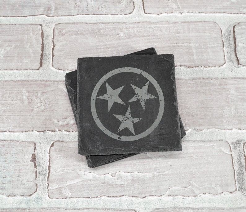 May include: A set of four black slate coasters featuring the state of Tennessee's official symbol, a circle with three white stars.