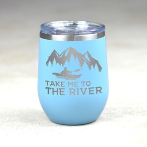 Puede incluir: Un vaso de acero inoxidable azul claro con una tapa blanca. El vaso tiene un gr&aacute;fico de una persona en kayak frente a monta&ntilde;as y &aacute;rboles. El texto "Take me to the river" est&aacute; impreso debajo del gr&aacute;fico.