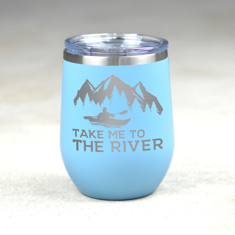 Puede incluir: Un vaso de acero inoxidable azul claro con una tapa blanca. El vaso tiene un gr&aacute;fico de una persona en kayak frente a monta&ntilde;as y &aacute;rboles. El texto "Take me to the river" est&aacute; impreso debajo del gr&aacute;fico.