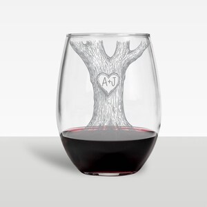 Puede incluir: Una copa de vino sin tallo transparente con un dise&ntilde;o de &aacute;rbol grabado en el lateral. El &aacute;rbol tiene un coraz&oacute;n tallado con las iniciales "A+J" en su interior.