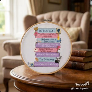 May include: A cross-stitch embroidery hoop featuring a stack of book titles from the Bridgerton series. The titles are in various colors, with floral and decorative accents. The hoop is set against a blurred background with books and furniture.
