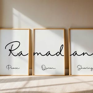 May include: Three framed art prints with gold frames. Each print has the word "Ramadan" in black script. Below each word is a smaller word: "Peace", "Quran", and "Sharing". The prints are on a white background.