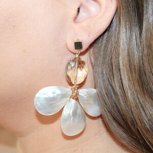 May include: Gold tone earrings with a large oval shaped clear crystal and three smaller white shell shaped crystals.